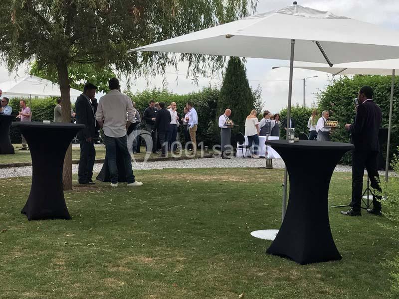 Groupe de personnes discutant dans un jardin sous des parasols, avec des tables hautes recouvertes de nappes noires.
