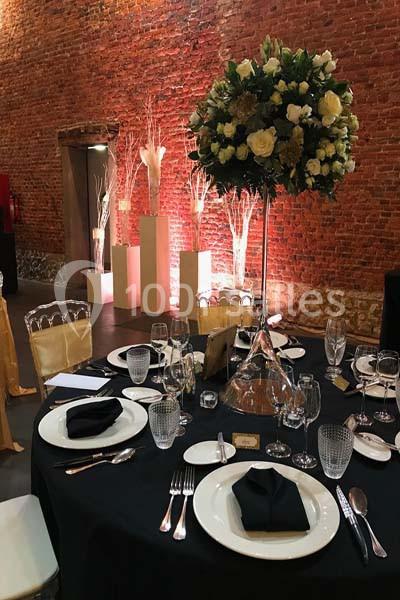 Table élégamment dressée avec nappes noires, vaisselle raffinée, serviettes pliées et centre de table floral.