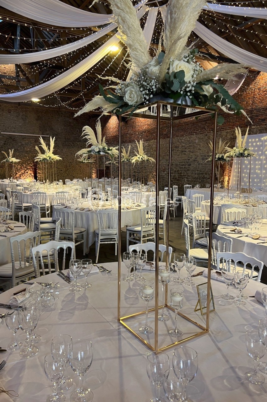 Salle de réception décorée avec des tables rondes, nappes blanches, chaises blanches et centres de table floraux élégants.