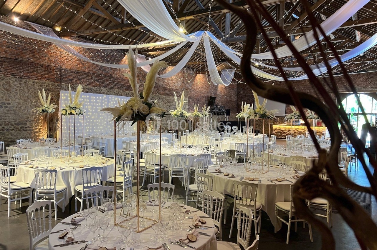Salle de réception décorée pour un mariage, avec tables rondes, nappes blanches et ornements floraux élégants.