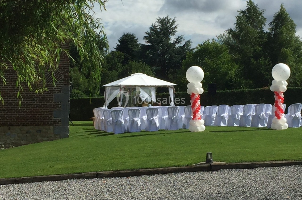 Chaises blanches alignées sous une tonnelle blanche dans un jardin, décorées de ballons rouges et blancs.