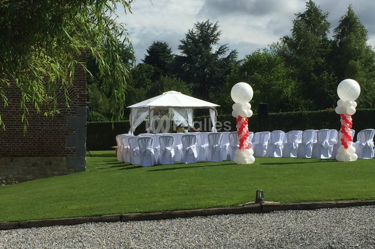 Chaises blanches alignées sous une tonnelle blanche dans un jardin, décorées de ballons rouges et blancs.