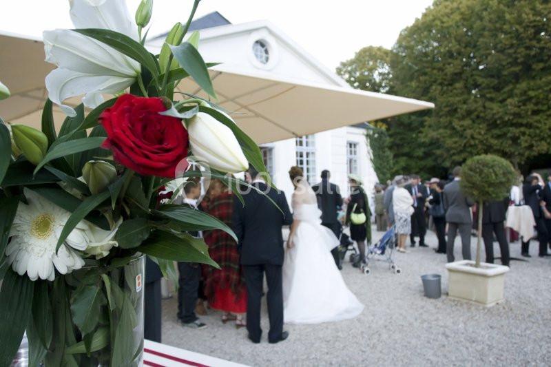 Un bouquet de fleurs en gros plan avec des invités rassemblés devant un bâtiment lors d'une réception en plein air.