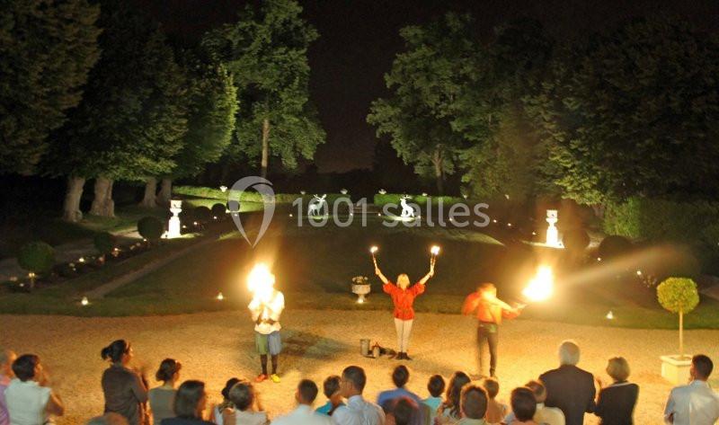 Spectacle nocturne avec des jongleurs de feu dans un jardin éclairé, observé par un public en plein air.