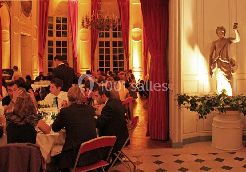Salle élégante éclairée, avec des convives dînant à des tables rondes et une statue décorative en arrière-plan.