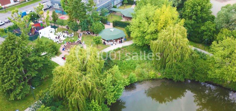Vue aérienne d'un parc avec un étang, des arbres, des espaces verts et des personnes rassemblées près d'une structure…