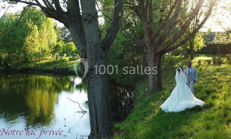 Un couple en tenue de mariage marche près d'un étang entouré d'arbres et de verdure au coucher du soleil.