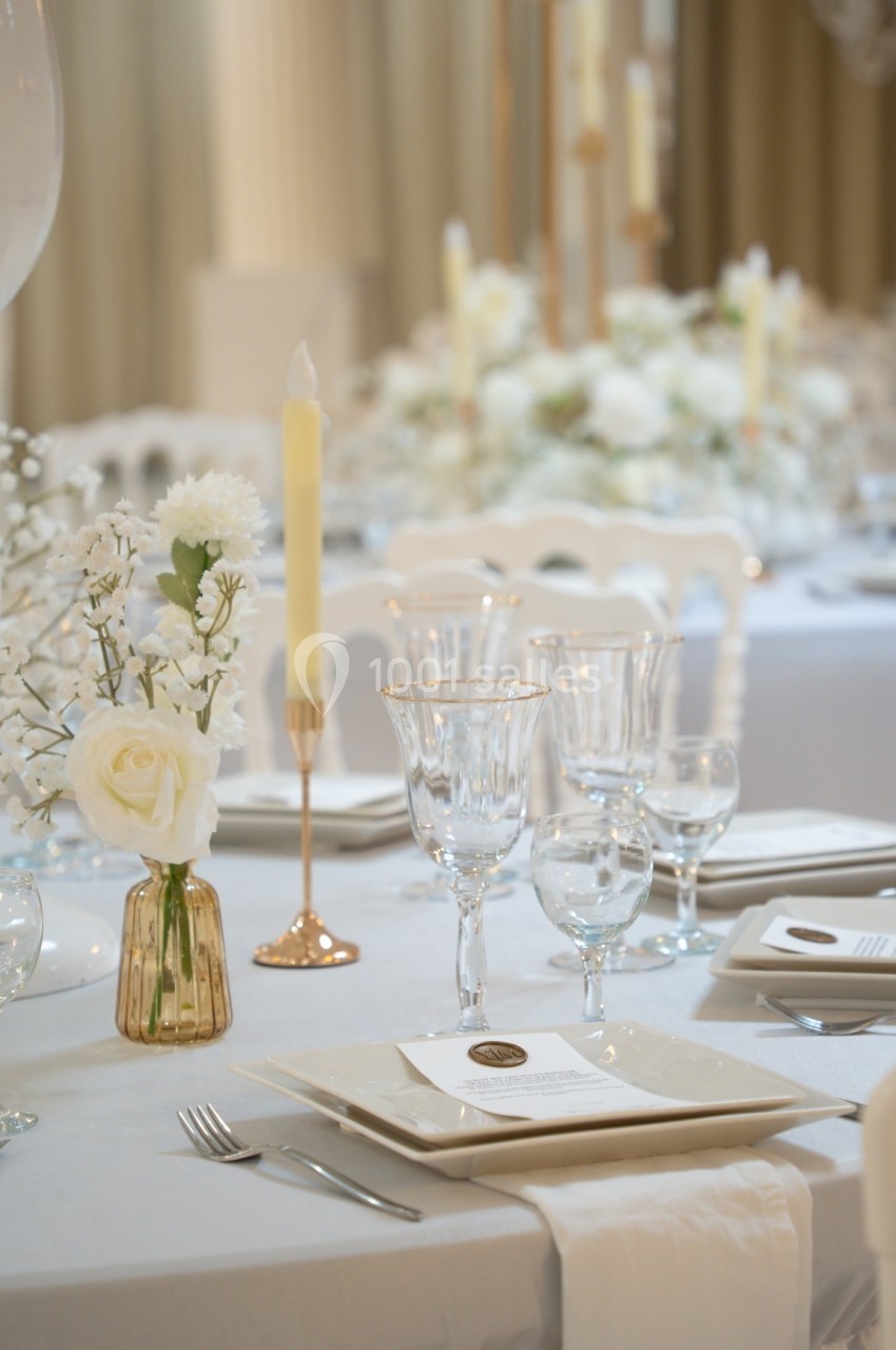 Table élégamment dressée avec vaisselle raffinée, bougies allumées et décoration florale blanche.