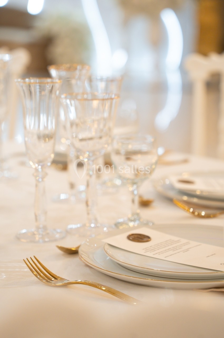 Table élégamment dressée avec assiettes blanches, couverts dorés, verres à pied et menus posés.