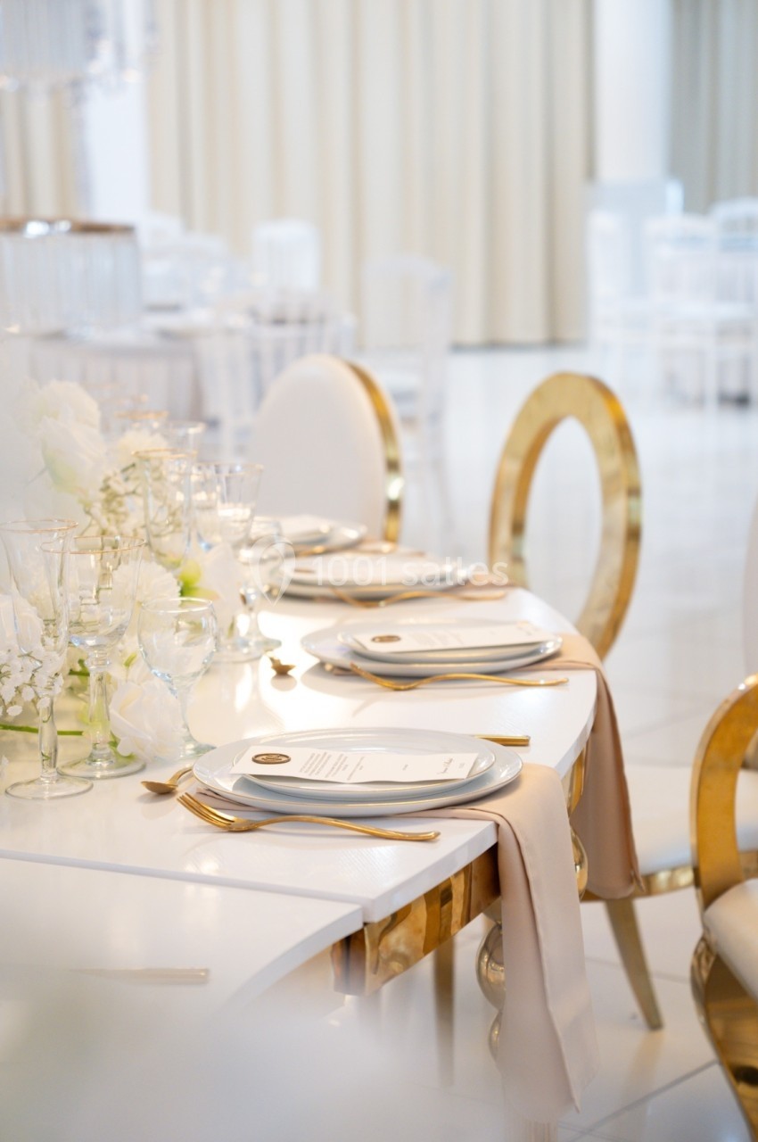 Table élégamment dressée avec vaisselle blanche, serviettes beiges et décorations florales dans une salle lumineuse.