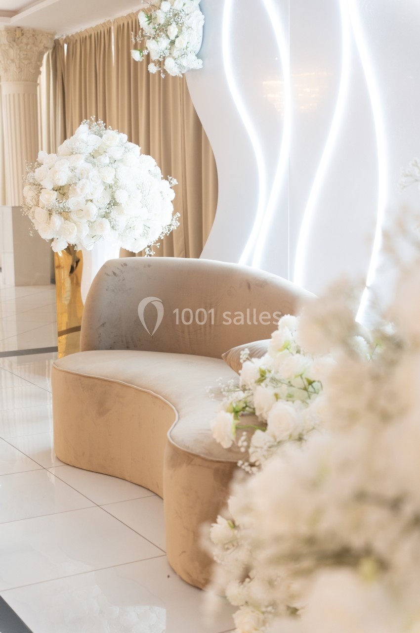 Canapé beige incurvé entouré de bouquets de fleurs blanches, dans un décor lumineux et élégant.