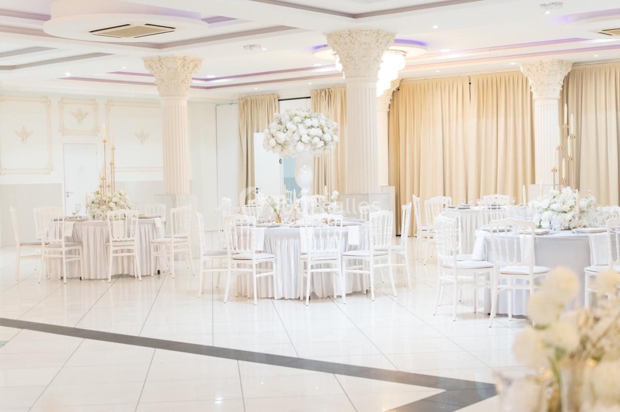 Salle de réception lumineuse avec tables rondes décorées de fleurs blanches et chaises blanches élégantes.