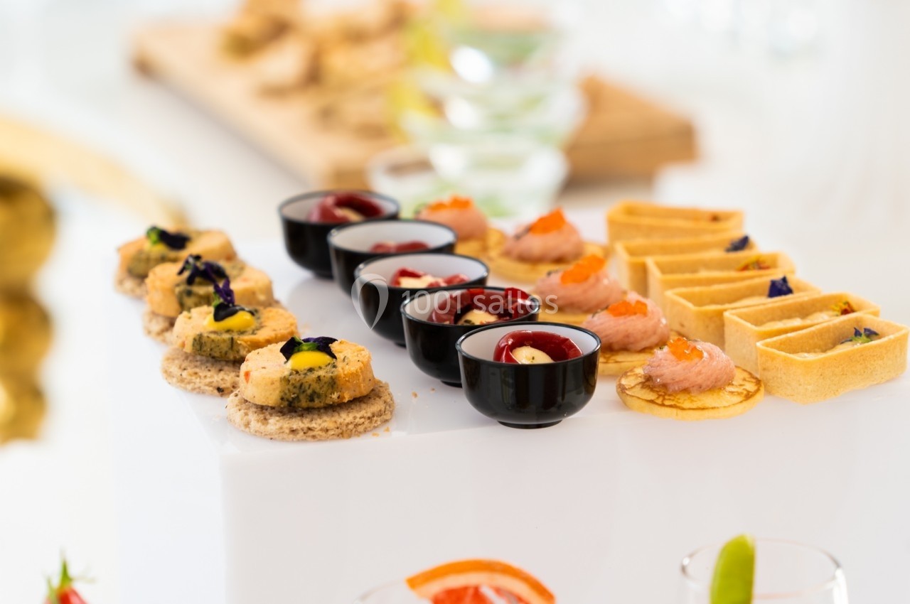 Assortiment de canapés et amuse-bouches variés présentés sur un plateau blanc lors d'un événement ou d'un buffet.