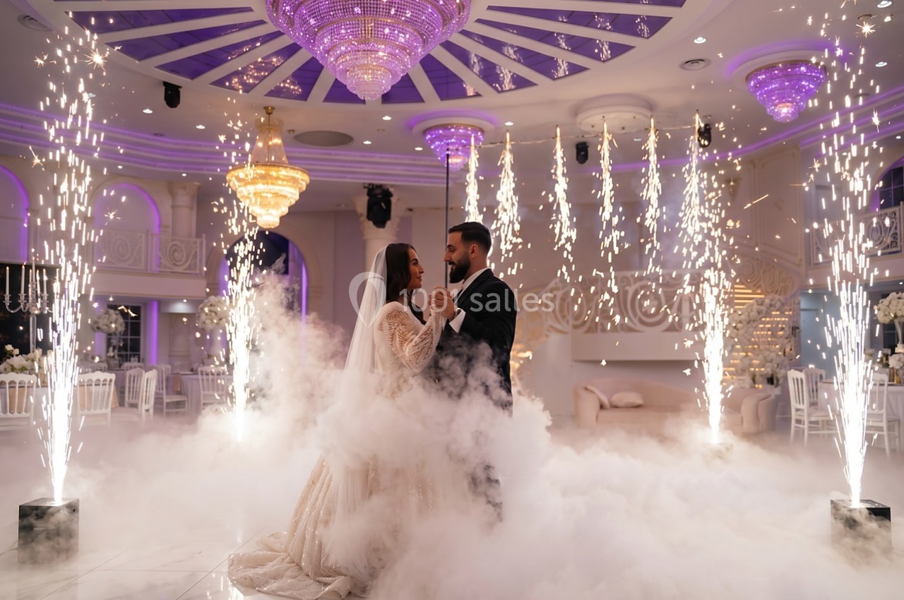 Un couple danse au milieu de la fumée et des étincelles dans une salle de réception ornée de lustres.