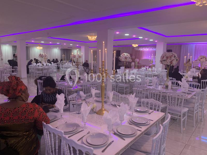 Salle de réception décorée avec des tables dressées, chandeliers dorés et éclairage violet.