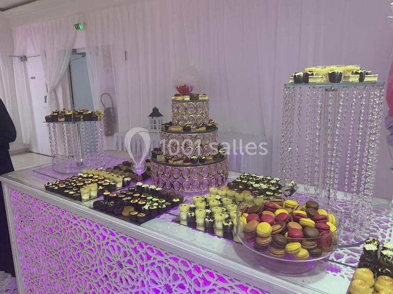 Buffet de desserts avec macarons colorés, verrines et pâtisseries disposés sur des présentoirs décoratifs dans une salle…