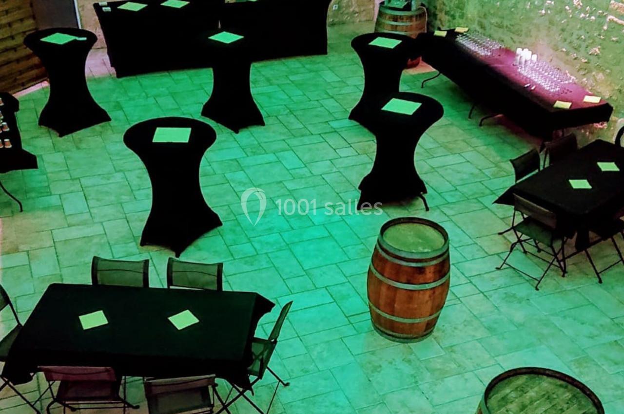 Salle aménagée avec des tables hautes et basses couvertes de nappes noires, éclairée par une lumière verte.