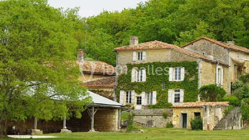 Maison en pierre recouverte de lierre, entourée d'arbres et située dans un cadre verdoyant.
