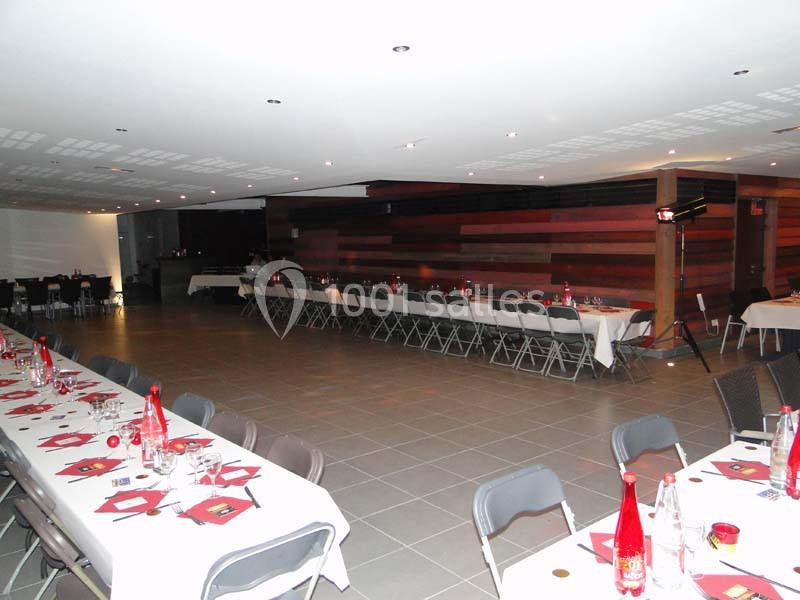 Salle de réception aménagée avec des tables dressées, chaises pliantes et éclairage tamisé.