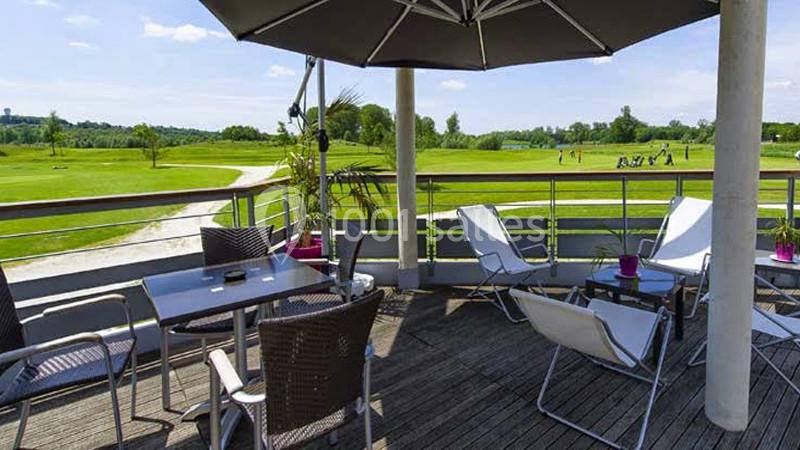 Terrasse en bois avec mobilier de jardin, parasol et vue sur un terrain de golf verdoyant par temps ensoleillé.