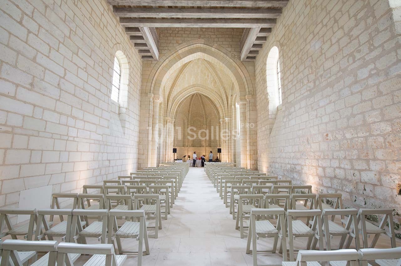 Intérieur d'une église en pierre avec des rangées de chaises en bois clair et une voûte en arrière-plan.