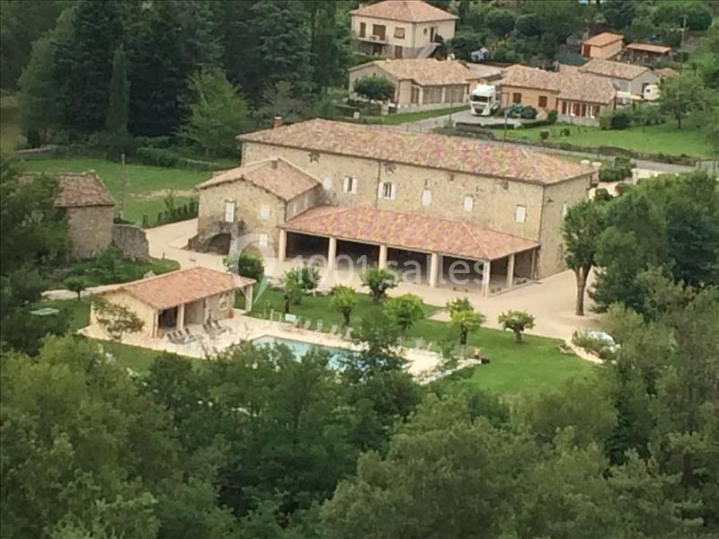 Vue aérienne d'une grande maison en pierre avec piscine, entourée de verdure et d'autres habitations.