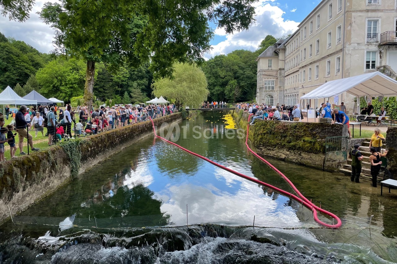 Un canal bordé d'arbres et d'un bâtiment historique, animé par un événement avec des stands et des visiteurs.