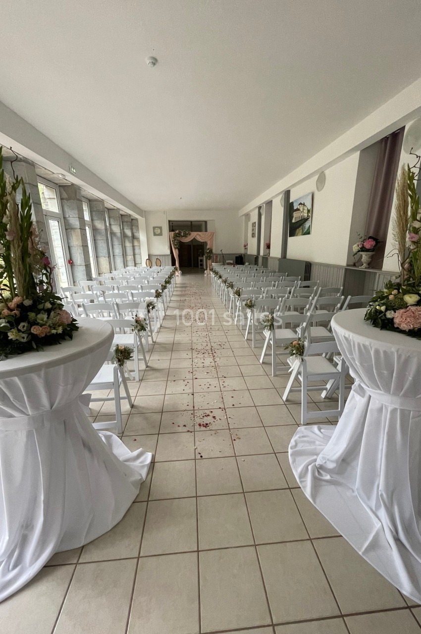 Allée centrale décorée pour une cérémonie, entourée de chaises blanches et de compositions florales.