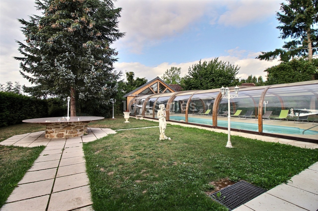 Jardin avec pelouse, statue, allée pavée, piscine couverte et arbres en arrière-plan.