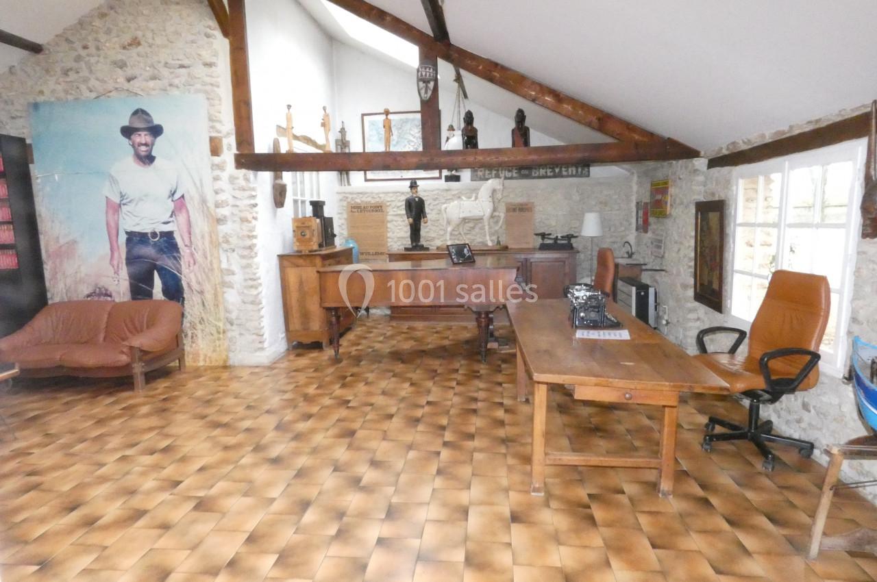 Bureau aménagé dans une pièce lumineuse avec murs en pierre, poutres apparentes et mobilier en bois.