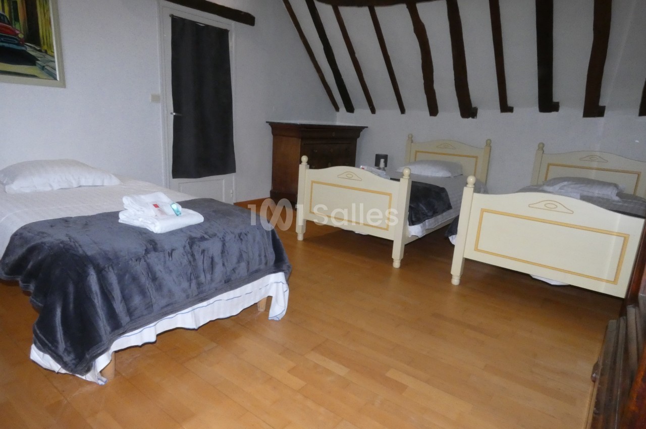 Chambre avec trois lits simples, parquet en bois, poutres apparentes et mobilier classique.