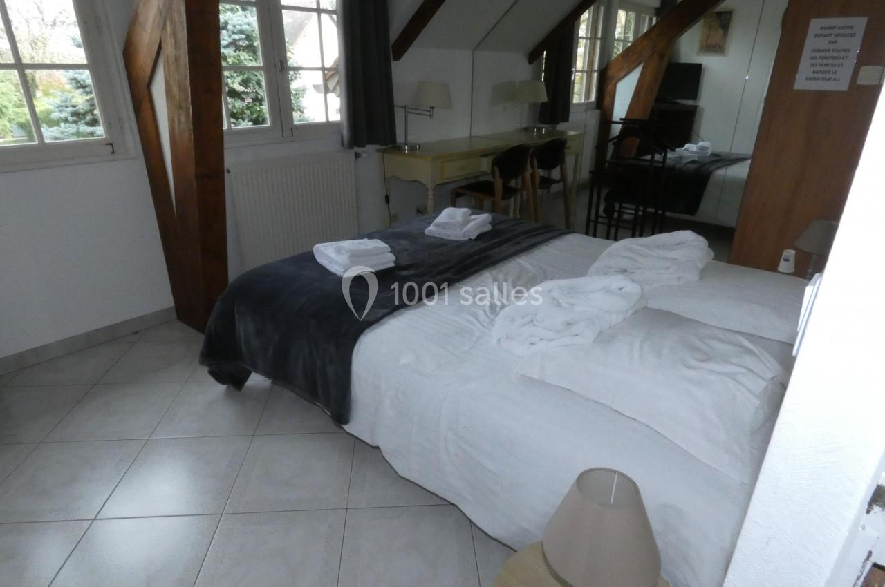 Chambre lumineuse avec lit double, draps blancs, peignoirs pliés, bureau en bois et fenêtres donnant sur un jardin.