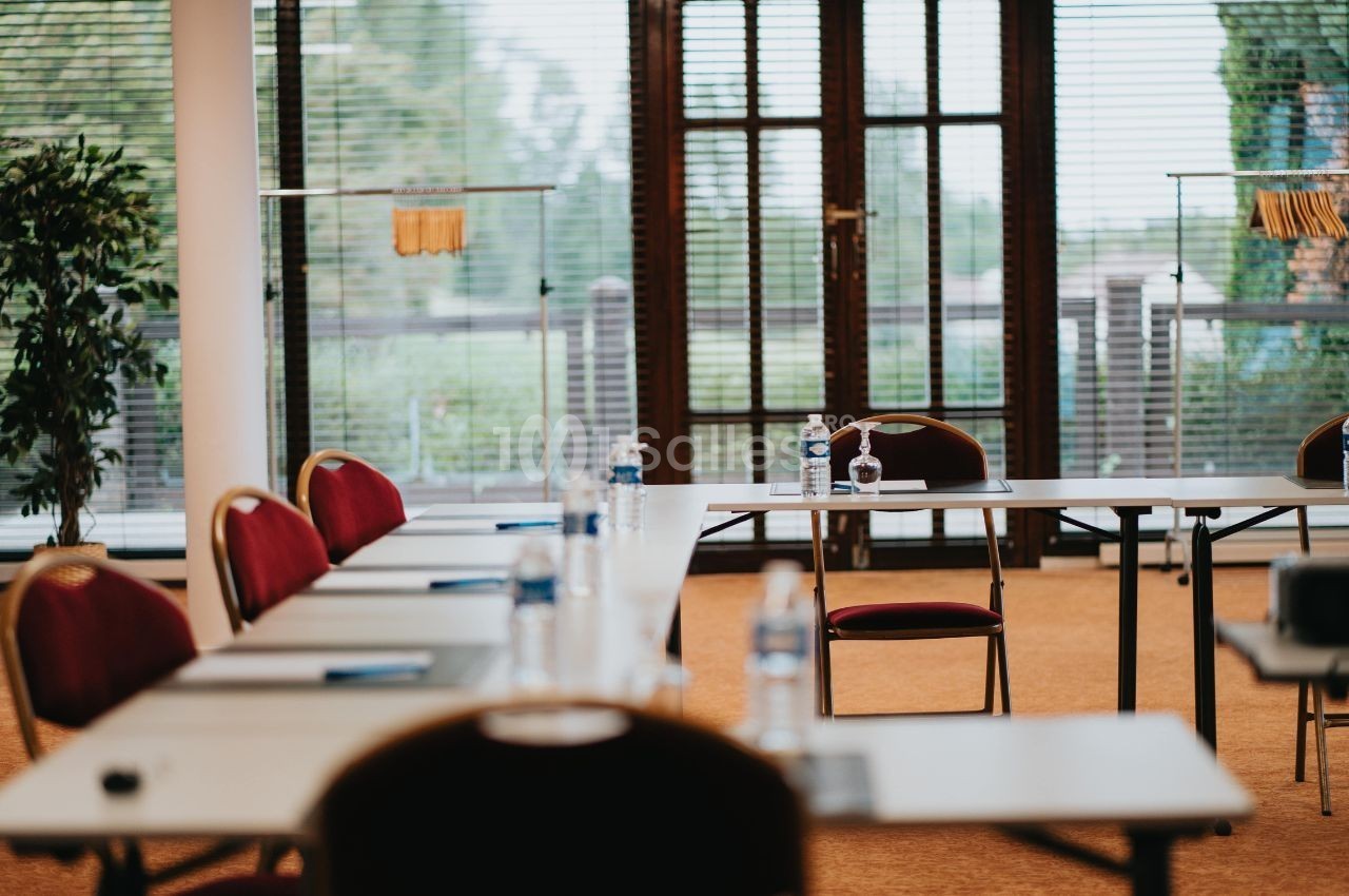 Salle de réunion lumineuse avec des tables blanches, des chaises rouges et des bouteilles d'eau sur les tables.