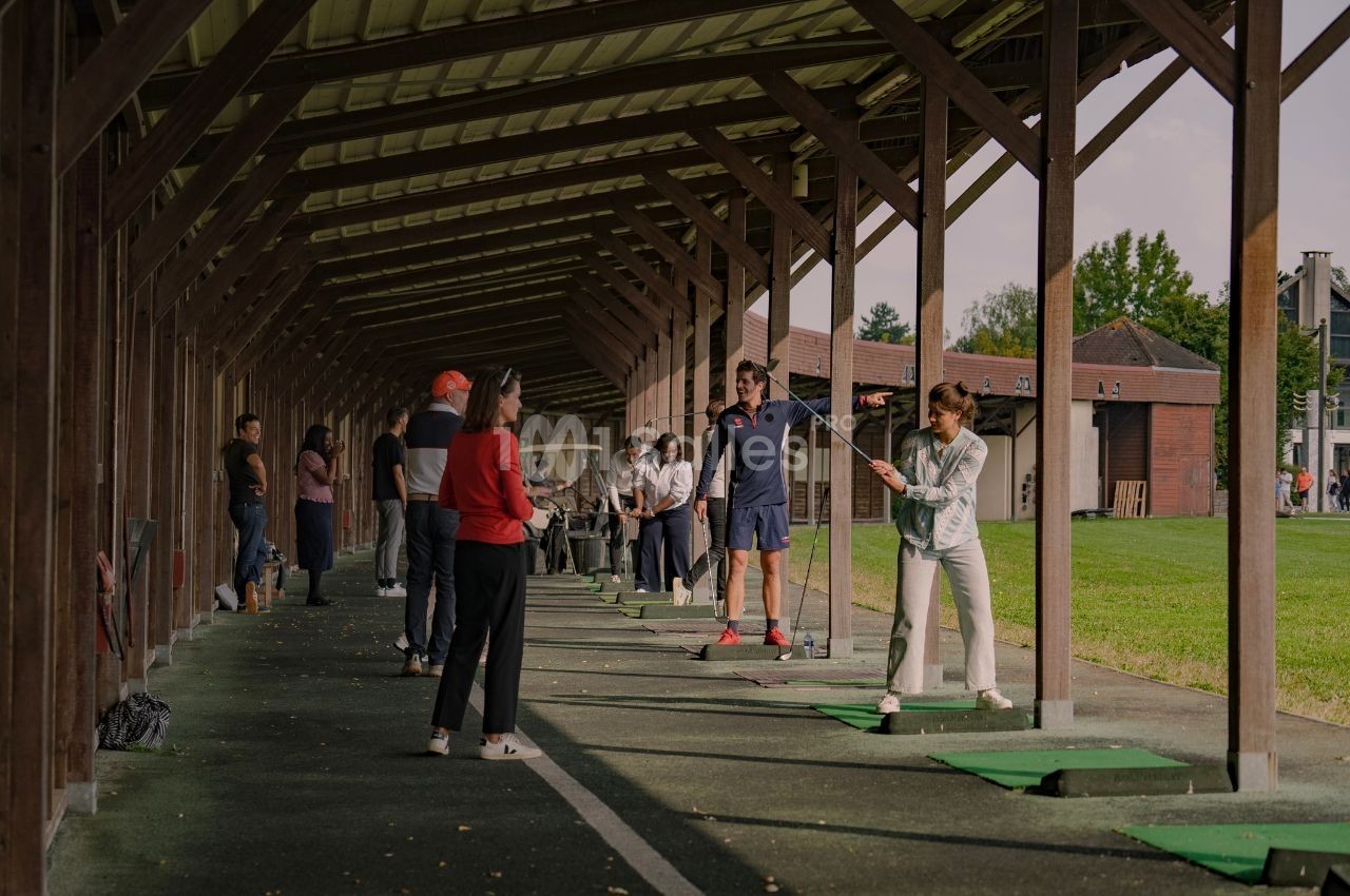 Des personnes s'entraînent au golf sous un abri, avec des instructeurs guidant les participants.