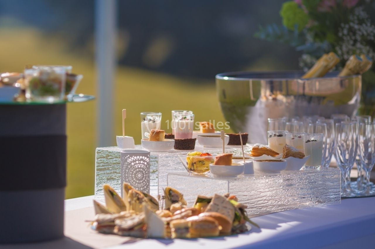 Table dressée avec des amuse-bouches variés, des desserts et des boissons, en extérieur sous une lumière naturelle.