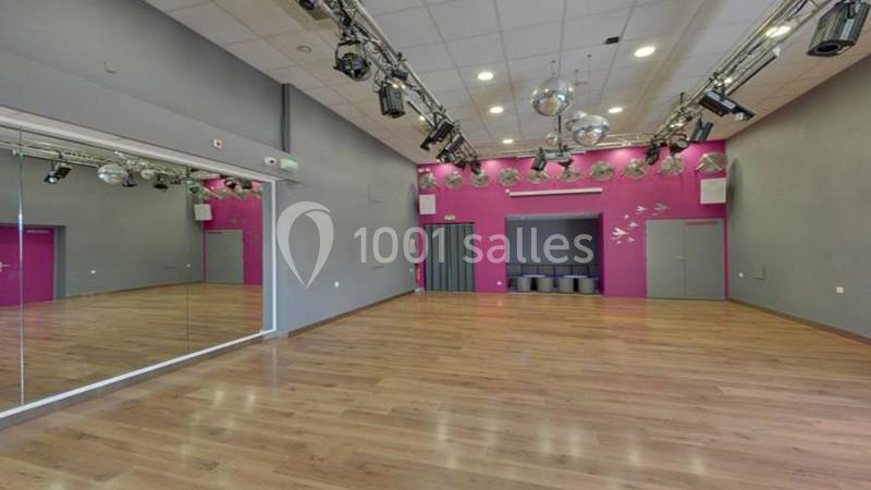 Salle de danse avec parquet, murs gris et roses, miroirs, projecteurs et boules à facettes suspendues au plafond.