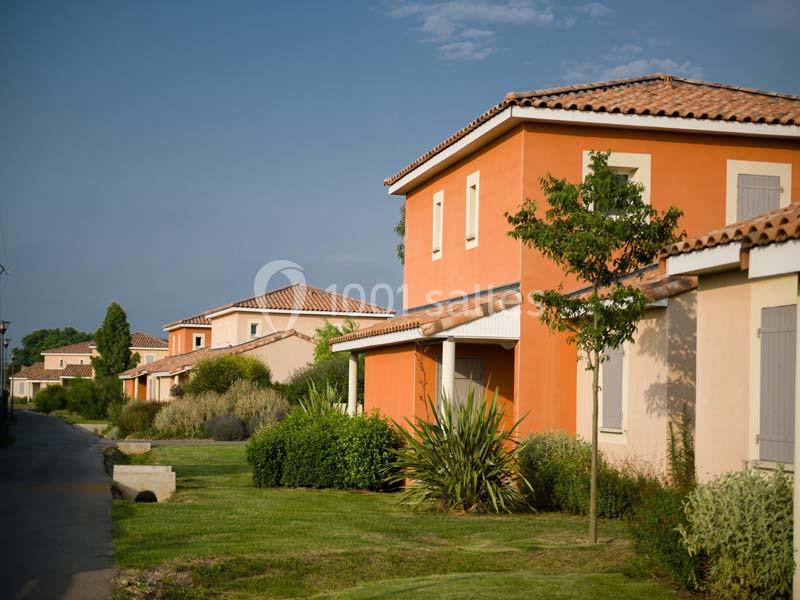 Maisons aux façades colorées avec toits en tuiles, entourées de jardins et d'une allée bordée de verdure.