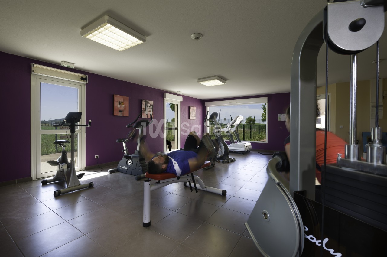 Salle de sport lumineuse avec équipements de fitness, un homme allongé sur un banc effectue un exercice.