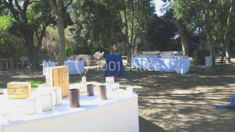 Tables décorées pour un événement en plein air dans un espace boisé, avec des objets et nappes blanches.