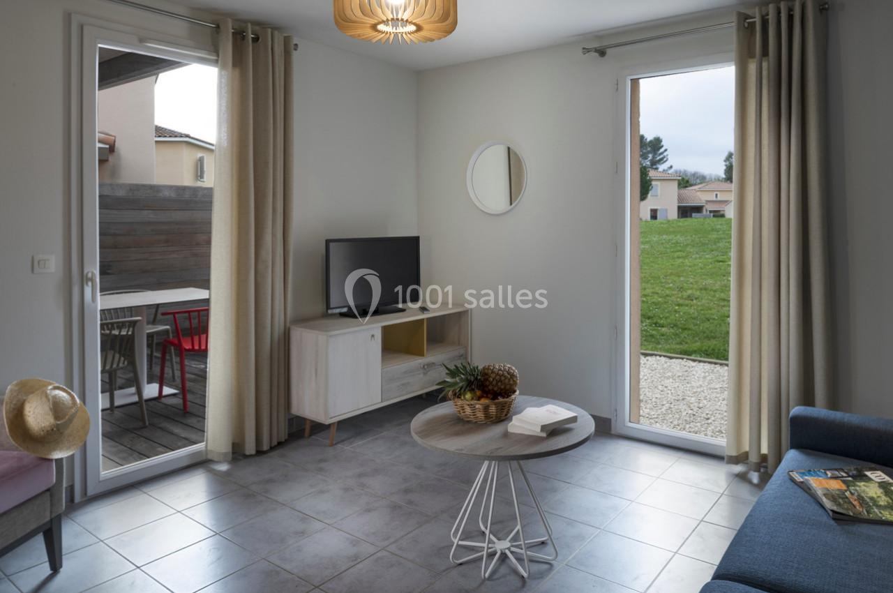 Salon lumineux avec table basse, canapé, télévision, terrasse extérieure et vue sur un jardin.