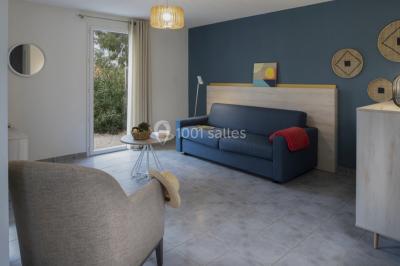 Salle à manger lumineuse avec table en bois, chaises colorées, cuisine ouverte et décoration sobre.