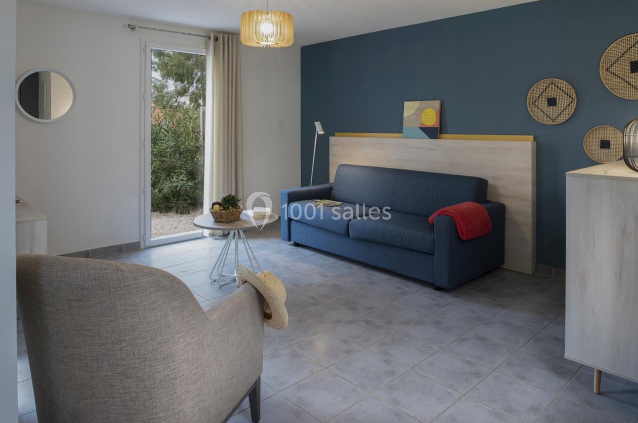 Salon lumineux avec canapé bleu, fauteuil beige, table basse ronde et décoration murale sur fond de mur bleu.