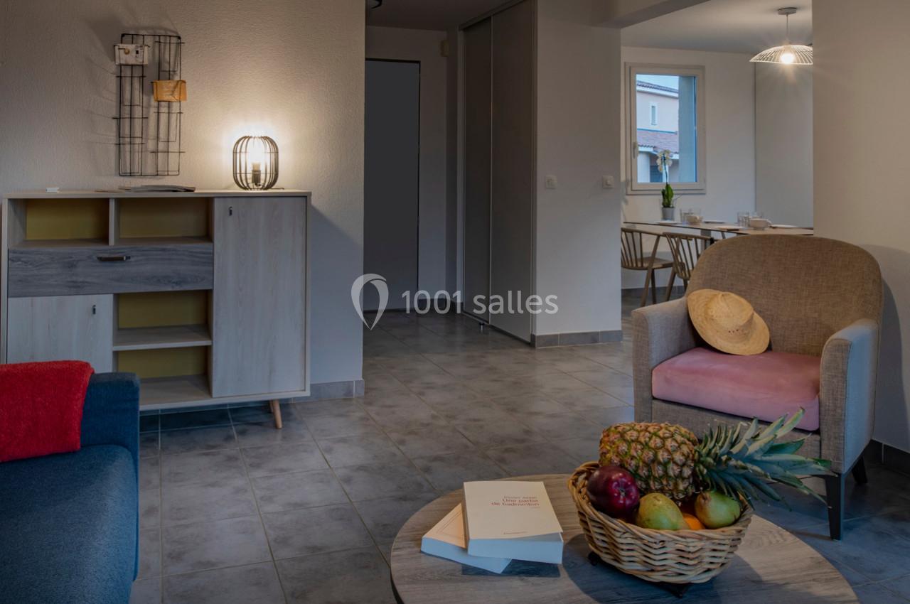 Salon avec mobilier moderne, corbeille de fruits sur une table basse, vue sur une salle à manger en arrière-plan.