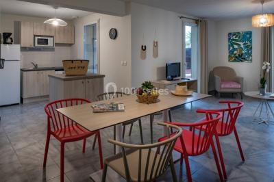 Salle à manger lumineuse avec table en bois, chaises colorées, cuisine ouverte et décoration sobre.