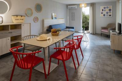 Salle à manger lumineuse avec table en bois, chaises colorées, cuisine ouverte et décoration sobre.