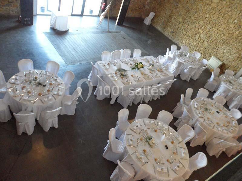 Salle de réception avec tables rondes et rectangulaires dressées, nappes blanches et décorations élégantes.