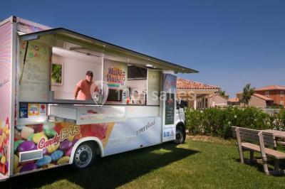 Salle à manger lumineuse avec table en bois, chaises colorées, cuisine ouverte et décoration sobre.