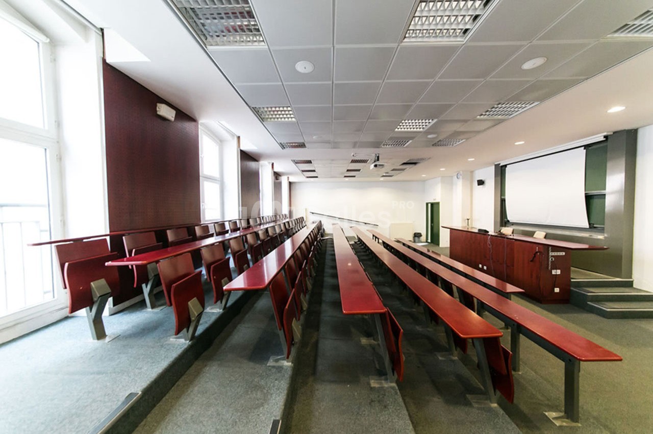 Salle de conférence vide avec rangées de bancs en bois, un projecteur et un tableau blanc à l'avant.