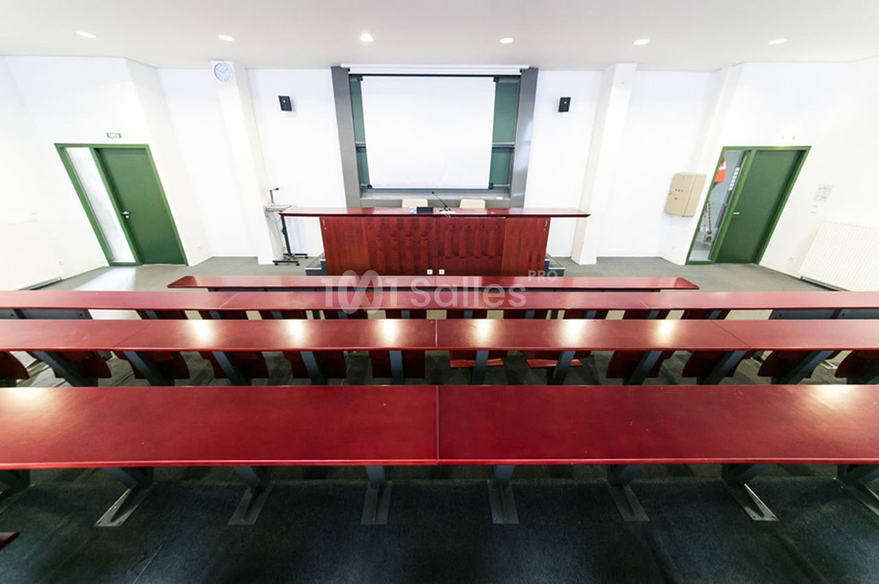 Salle de conférence vide avec rangées de bancs en bois, un pupitre et un écran de projection à l'avant.