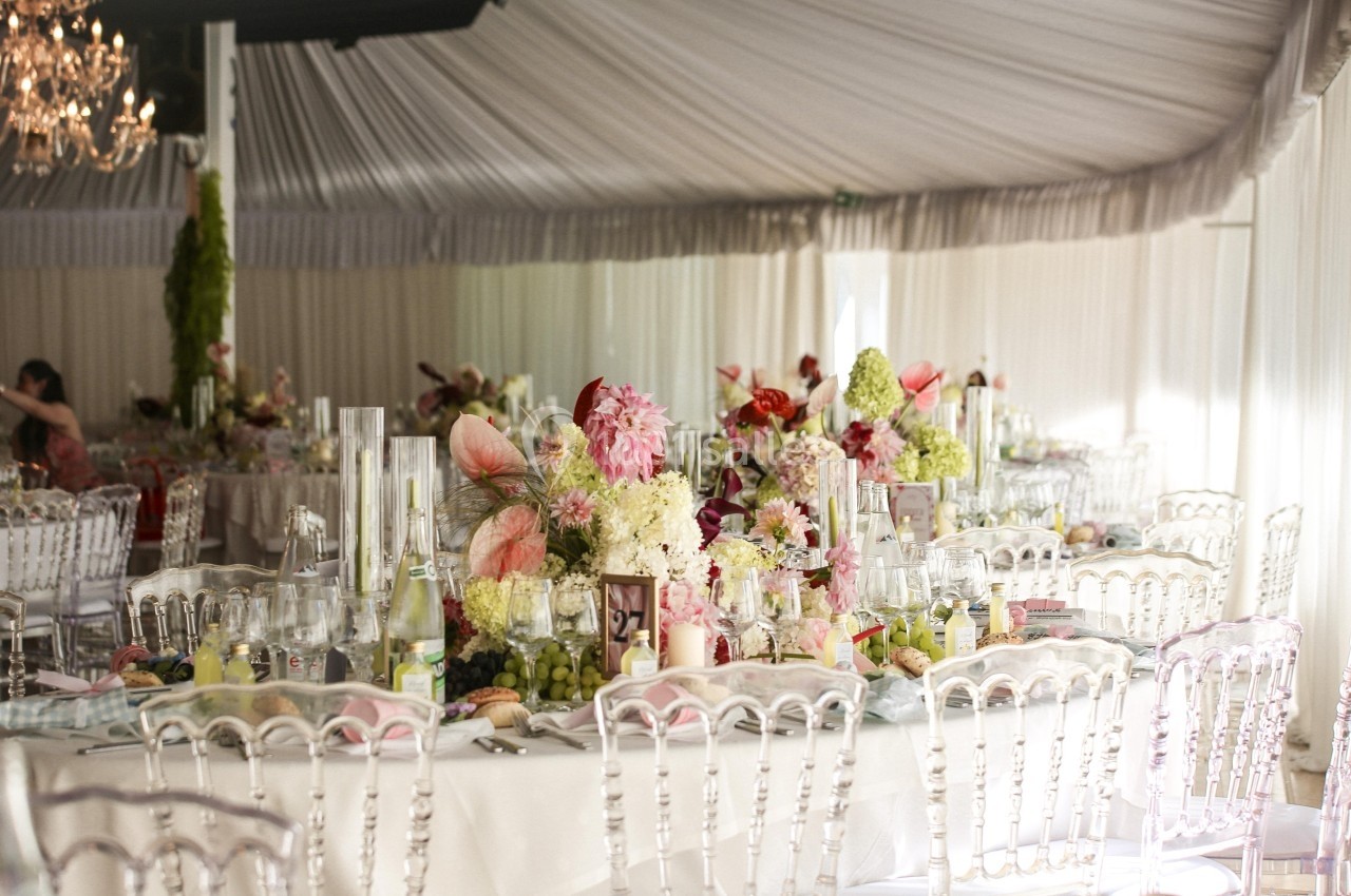 Tables élégamment décorées avec des fleurs colorées et des chaises transparentes dans une salle de réception lumineuse.